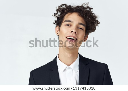 Cute curly man in a dark suit on a gray background office worker