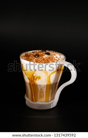 Hot chocolate or coffee beverage in glass cup with holder, isolated on black. Visible coconut crumbs, milk, whipped cream and other sweet ingredients. Caramel