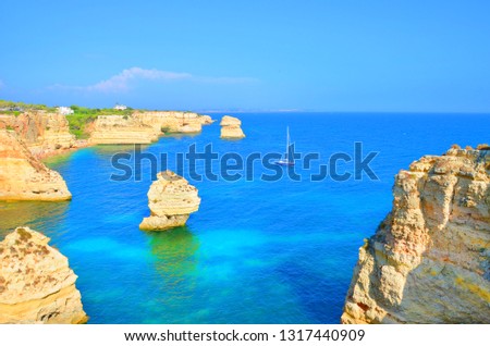 Amazing seascape with beautiful sea rocks and a sailing boat taken in summer season in portuguese Algarve near city Lagoa. The area is popular for its beautiful sceneries and sea caves. 