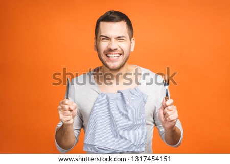 Young hungry crazy man holding a fork and a knife. Isolated on orange background. Royalty-Free Stock Photo #1317454151
