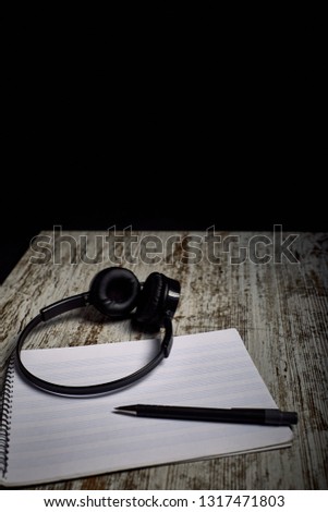 composition of black headphones next to an empty pentagram notebook on a wooden table