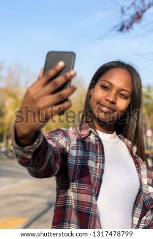 Young african american woman standing outdoors while taking a selfie in sunny day