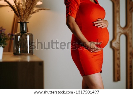 pregnant woman in a red dress. He keeps his hands on his stomach.