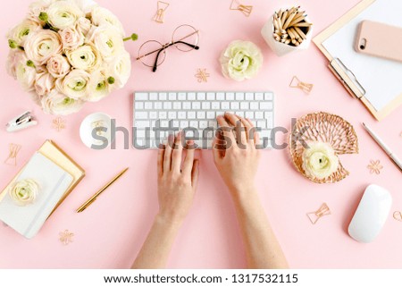 Stylized, pink women's home office desk. Workspace with female hands, computer, bouquet ranunculus and roses, clipboard, feminine golden fashion accessories isolated on pink background. Flat lay. Top 