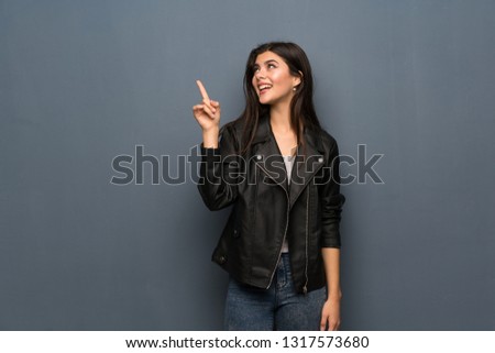 Teenager girl over grey wall intending to realizes the solution while lifting a finger up