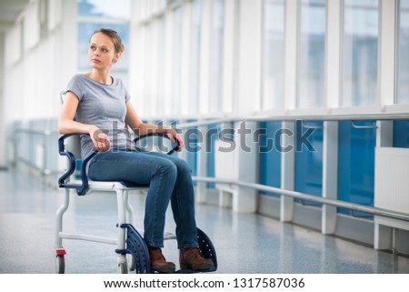 Female patient, sitting in a wheelchair for patients feeling not well enough to stand, waiting to be taken care of in a modern hospital (shallow DOF; color toned image)