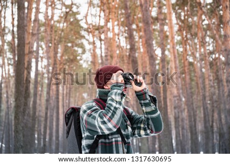 Hiking male person in winter forest taking photograph. Man in checkered winter shirt in beautiful snowy woods uses old film camera