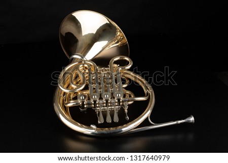 French horn on a wooden table. Beautiful polished musical instrument. Dark background.