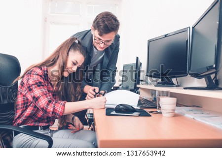 Young smart man pointing with pen on paper showing information to young female woman  colleague working in team.
