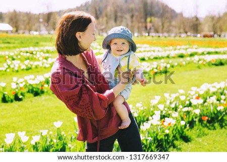 Loving mother and baby girl among yellow tulips flowers. Woman with her daughter playing outdoors in spring park. Family on nature. Image of Mother's Day, Easter. Tulip field in Arboretum, Slovenia.