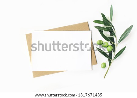 Feminine stationery, desktop mock-up scene. Blank horizontal greeting card and craft envelope with olive branch.White table background. Flat lay, top view. 