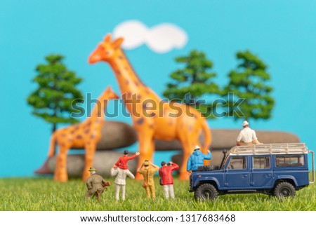 Miniature toys of a group of people on safari trip watching giraffes - a hunter, father and son on shoulder ride, photographer with an off road transport on grassland.