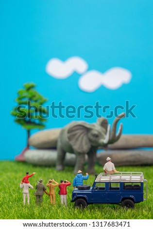 Miniature toys of a group of people on safari trip watching loxodonta african elephant - a hunter, father and son on shoulder ride, photographer with an off road transport on grassland.