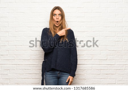 Blonde woman over brick wall surprised and pointing side