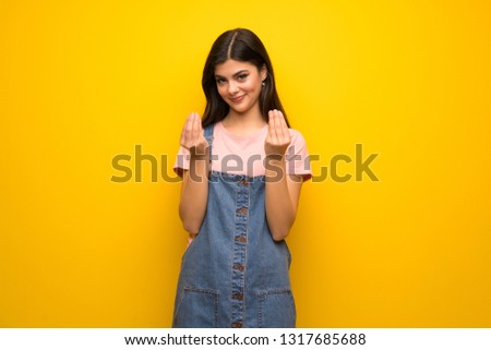 Teenager girl over yellow wall making money gesture