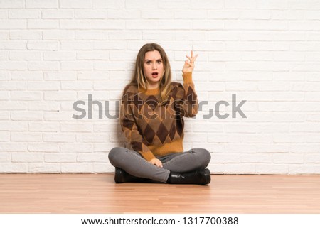 Teenager girl sitting on the floor surprised and shocked while looking right