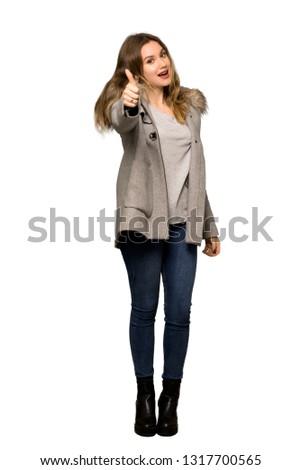 A full-length shot of a Teenager girl with coat giving a thumbs up gesture because something good has happened on isolated white background
