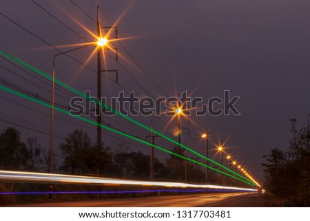 Low view, colorful light, car headlights with lamps and dark and trees and electric poles on the side of Thai rural roads.