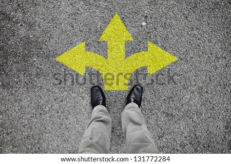 A pair of feet standing on a tarmac road with yellow arrow print pointing in three different directions for the concept of making decision at the crossroad. Royalty-Free Stock Photo #131772284