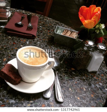 A coffee cup sits untouched on a granite table with pretty flowers and full place setting. 