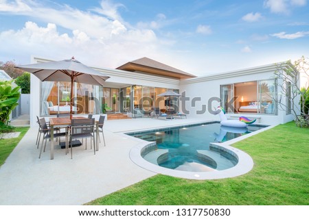 real home or house  Exterior design showing tropical pool villa with greenery garden, sun bed, umbrella, pool towels and colorful floating unicorn Royalty-Free Stock Photo #1317750830