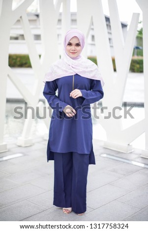 Portrait of a beautiful Asian woman  wearing dark blue color dress and pants with hijab in a real environment. Muslim female hijab fashion portraiture concept.