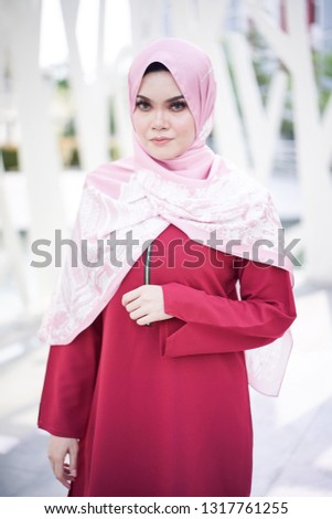 Portrait of a beautiful Asian woman  wearing red color dress and pants with pink hijab in a real environment.  Muslim female hijab fashion portraiture concept.
