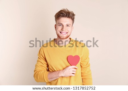 Portrait of young man with paper heart on color background