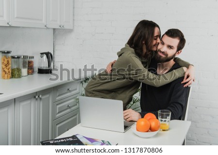 beautiful smiling young woman hugging and kissing man using laptop during breakfast in kitchen 