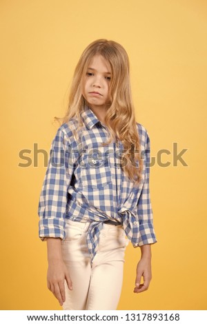 Child pose in shirt and pants on orange background. Child with cute face and long blond hair.
