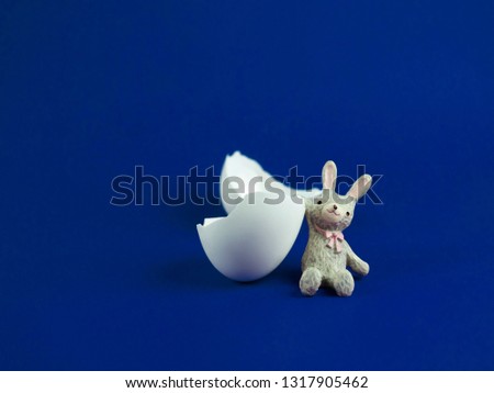 Cute rabbit doll with egg shell broken crack on blue background, Easter concept