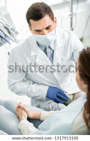 selective focus of dentist in mask looking at woman in dental clinic