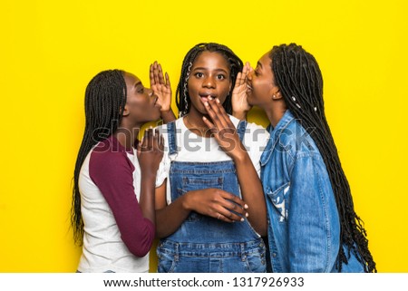 Portrait of thoughtful minded african girl with long hair listening gossips from friends in two ears holding hand on chin isolated on bright yellow background