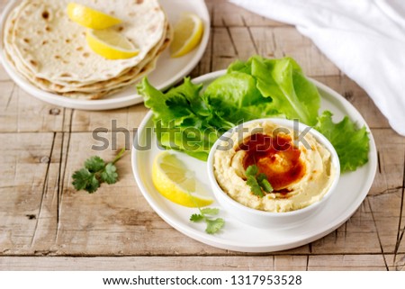 Hummus with olive oil and paprika, served with pita, lemon and lettuce leaves.