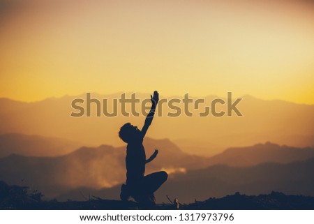Man sitting and lift hands to sky for worshipping God at sunset background. christian silhouette concept.