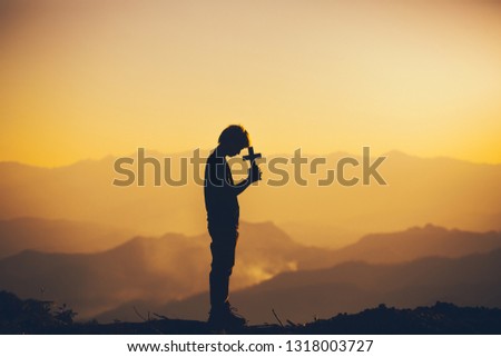 Young man standing praying with holding christian cross at sunset background. christian silhouette concept.