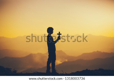 Young man standing praying with holding christian cross for worship God at sunset background. christian silhouette concept.