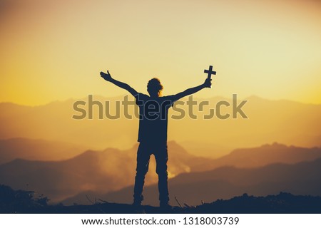 Man standing holding christian cross for worshipping God at sunset background. christian silhouette concept.