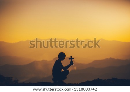 Young man sitting praying with holding christian cross at sunset background. christian silhouette concept.