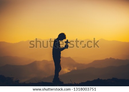man standing praying with holding christian cross at sunset background. christian silhouette concept.