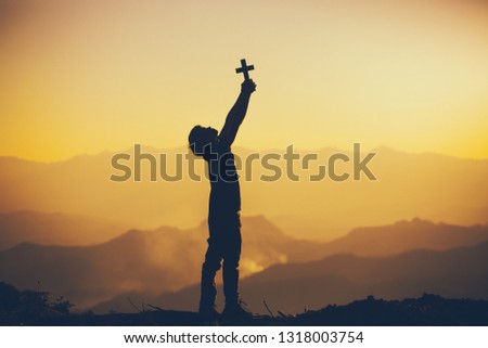 Young man standing holding christian cross for worshipping God at sunset background. christian silhouette concept.
