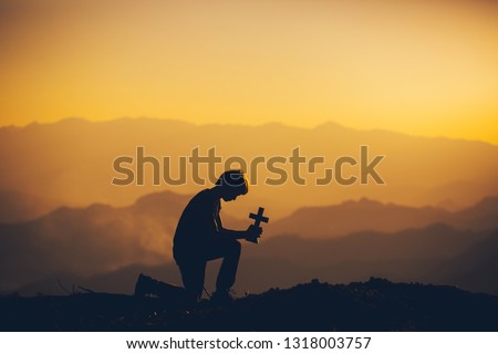 Young man sitting down and praying to God at sunset background. christian silhouette concept.