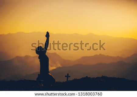 Young man kneeling down and praying at sunset background. christian silhouette concept.