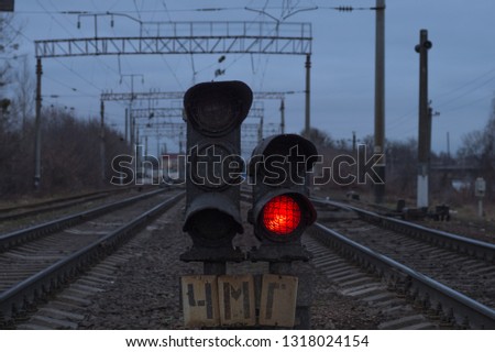 Red signal of the railway traffic light. Gray industrial railway background. On the right and on the left there are railway lines, in the center a traffic light is glowing with bright red light.