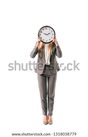 businesswoman in suit holding clock in front of the face, isolated on white