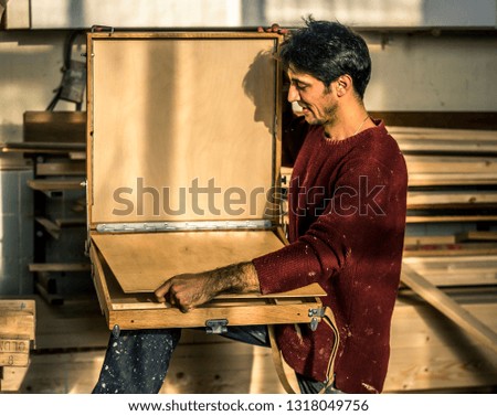 Portrait of an artist who is making this easels in his studio in Moscow, Russia. Talented armenian man in bordo swetshirt.