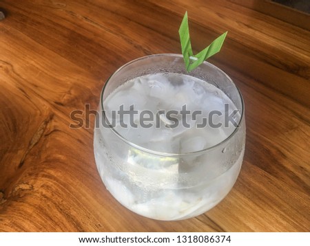 Glass of fresh coconut juice, drink coconut water naturally cool. Indonesian Ice coconut drink or es kelapa muda on glass with leaf in isolated wooden background
