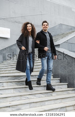Full length image of trendy couple man and woman 20s in warm clothes walking down gray stairs outdoor