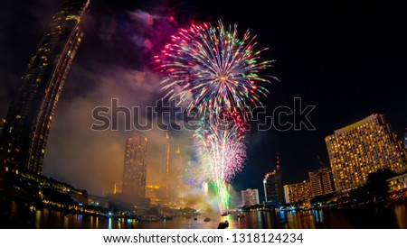 A large firework welcomes the new year at night, arranged in the middle of the river. Lots of people are interested Gives a feeling of excitement and wonder among the many skyscrapers.