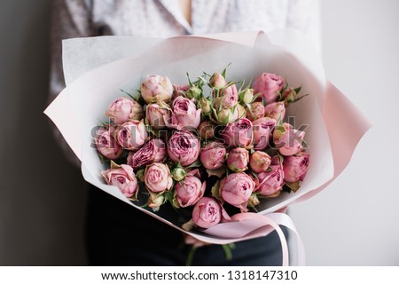 Very nice young woman holding big and beautifu mono bouquet of fresh pink roses on the grey wall background 